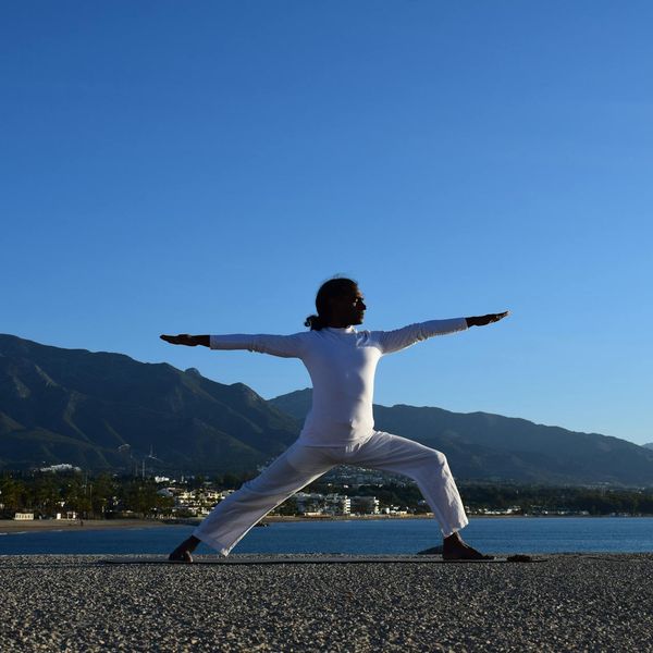 Silhouette of a person in a strong yoga warrior pose at sunrise.